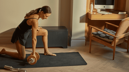 Woman performing a dumbbell exercise on a mat beside a Fittle Box in a home office setting.
