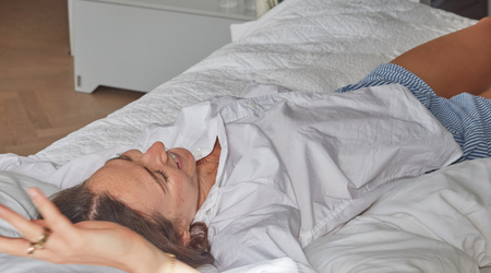 Woman lying in bed feeling fatigued, illustrating the choice between rest and exercise.