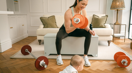 Woman performing a barbell squat with Fittle weights in a living room setting with her baby crawling nearby.