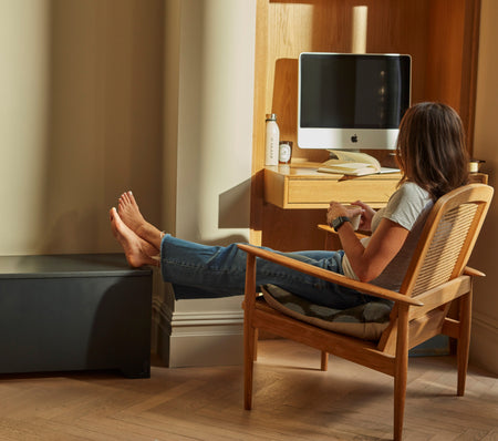 Person relaxing at a home workspace, seated in a wooden chair with feet up, reflecting a balanced approach to work, recovery and everyday wellness