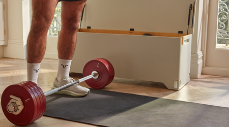 Man stands in home gym with Fittle barbell and weights at his feet.