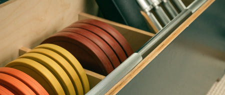 Close up detail shot of the inside of a midnight Fittle box, showing weight plates, bench mat, dumbbells and barbell.