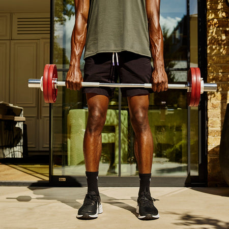 A man holding a Fittle Barbell with two 5kg plates on each side in a sunny patio setting. 