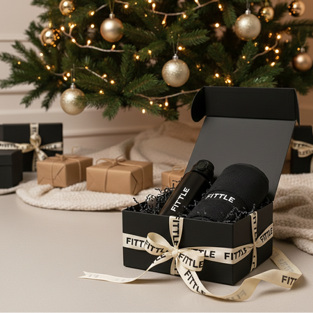 Black gift box with 'FITTLE' branding in front of a decorated Christmas tree.