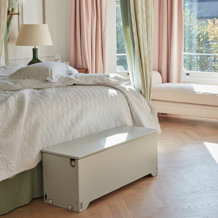 Soft grey Fittle Box home strength training storage bench placed at the end of a bed in a light-filled bedroom, showcasing design-led fitness equipment that doubles as elegant bedroom furniture
