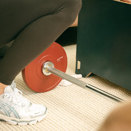 Close up of Fittle barbell with weight plates beside the Fittle Box storage bench during a home workout