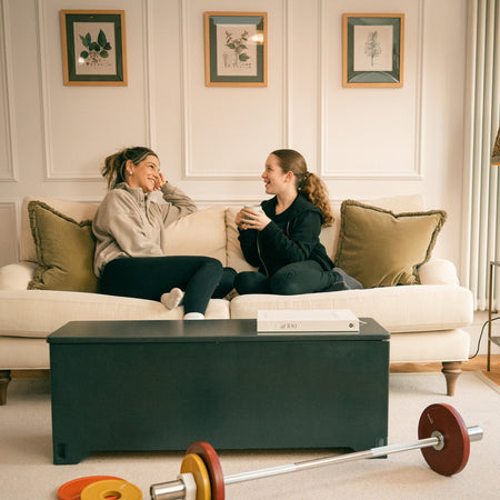 Fittle Box home gym with barbell and weight plates in a stylish UK living room while a mum and daughter relax on a sofa after a home strength training workout