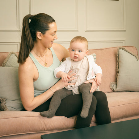 Woman sitting on sofa holding baby in a modern living room with Fittle Box home gym bench nearby