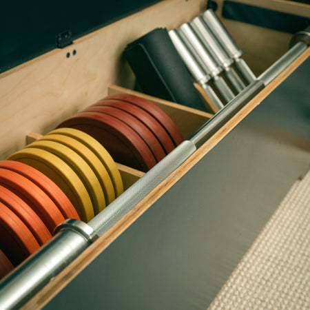 Barbell and weight plates neatly stored inside the Fittle Box all in one home gym bench