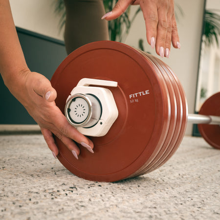 Close up of a person loading a barbell with 4 Fittle 5kg weight plates in a home setting.