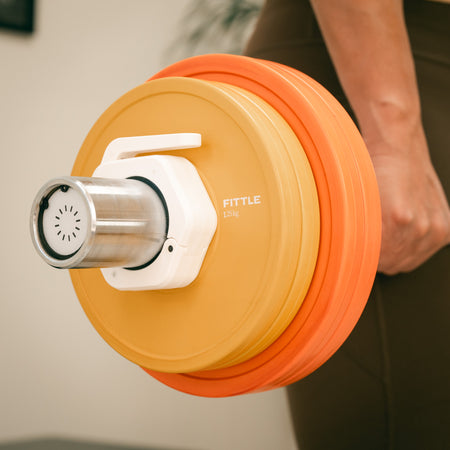 Close up of a person holding a Fittle Barbell with orange and yellow weight plates.