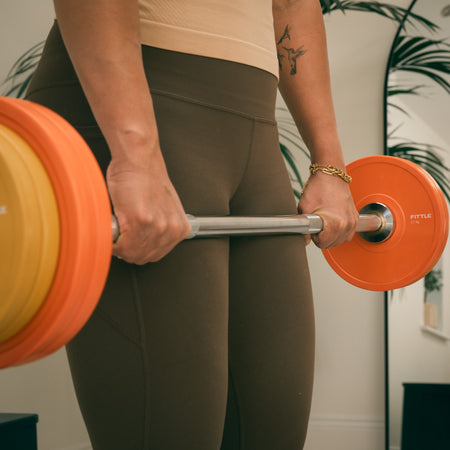 Person lifting a Fittle barbell with orange weights in a home setting 
