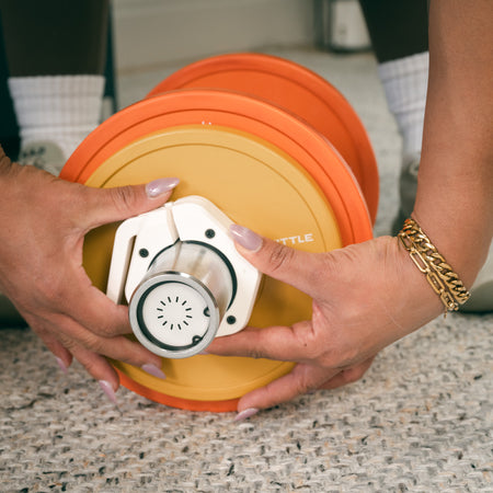 Close-up image of a person securing a Fittle adjustable dumbbell with a white bar collar. 