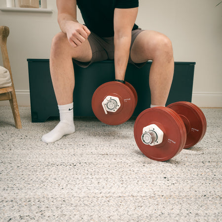 Person sitting on a Fittle box with two adjustable Fittle dumbbells in a modern home setting.