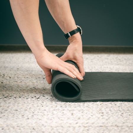 Person rolling up a Fittle Bench Mat on a speckled floor.
