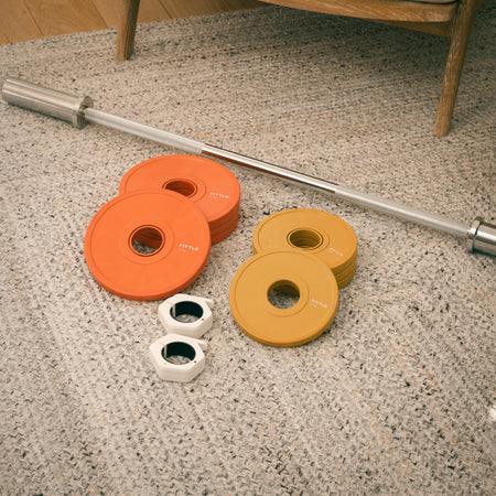 Barbell with orange and yellow weight plates and collars on a speckled floor.