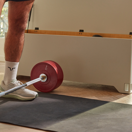Closeup of Fittle barbell with red weights on a a Fittle mat in front of  Fittle Box in a home setting.